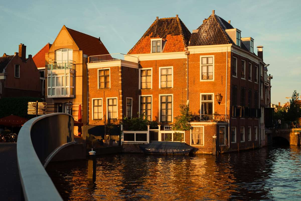 Brick canal houses glowing in warm golden-hour light beside calm water in Leiden